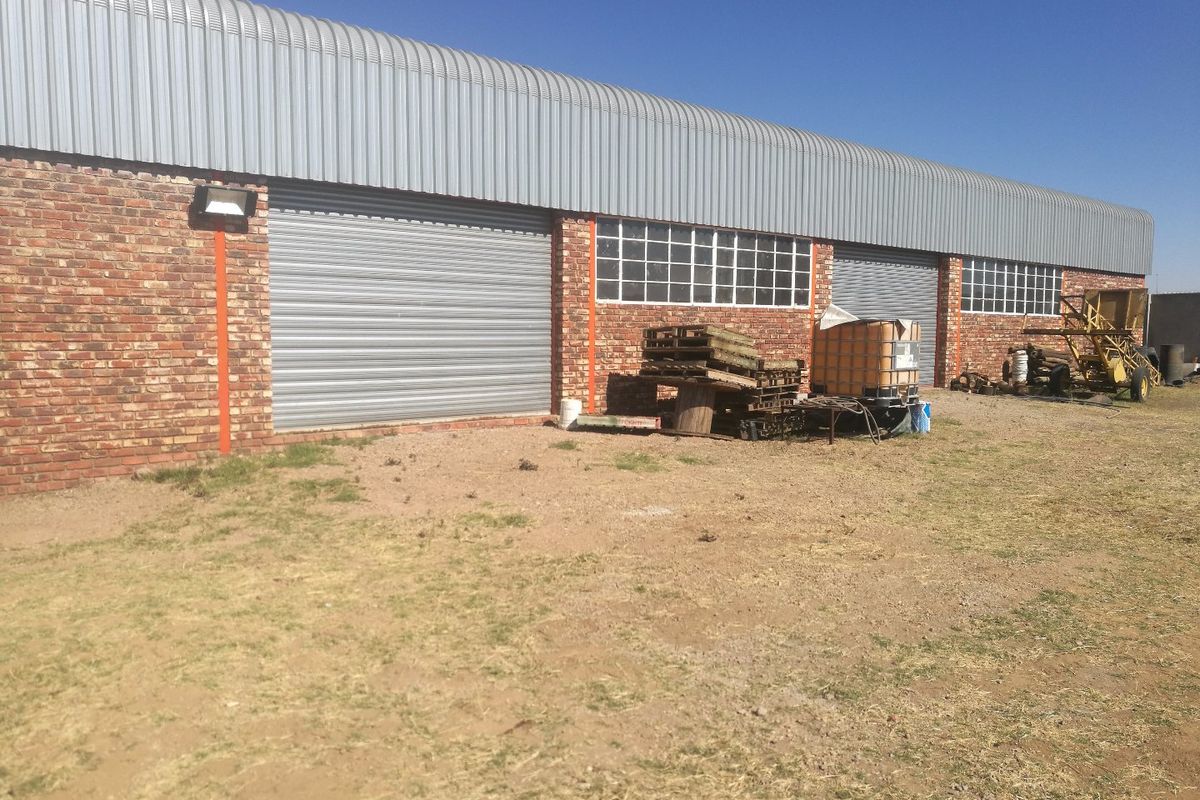 Rear view of an industrial warehouse building featuring face brick walls, corrugated metal roofing, and multiple roller shutter access doors.