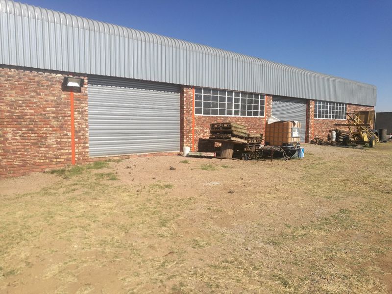 Rear view of an industrial warehouse building featuring face brick walls, corrugated metal roofing, and multiple roller shutter access doors.