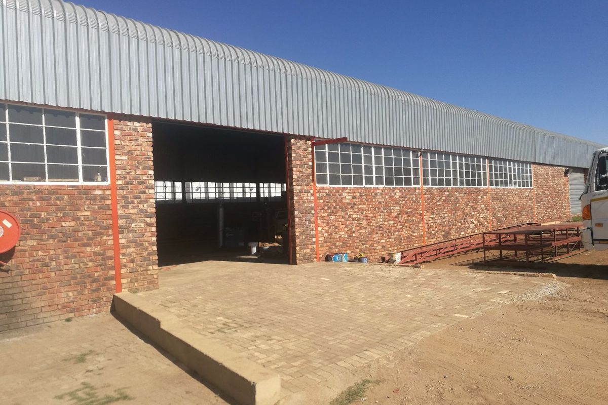 Industrial warehouse exterior featuring a corrugated metal roof, exposed brick facade, large entrance, and a paved loading area.
