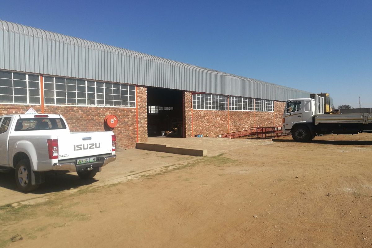 Industrial warehouse facility featuring exposed brickwork, corrugated metal roofing, and large loading bay access, situated on a spacious unpaved yard.
