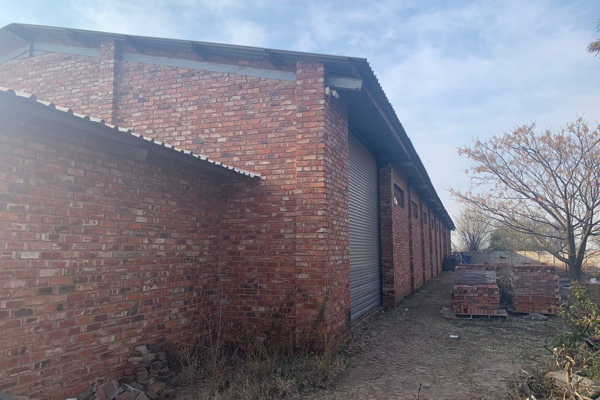 Exterior view of an industrial brick warehouse building featuring a metal roller shutter door and corrugated roofing.