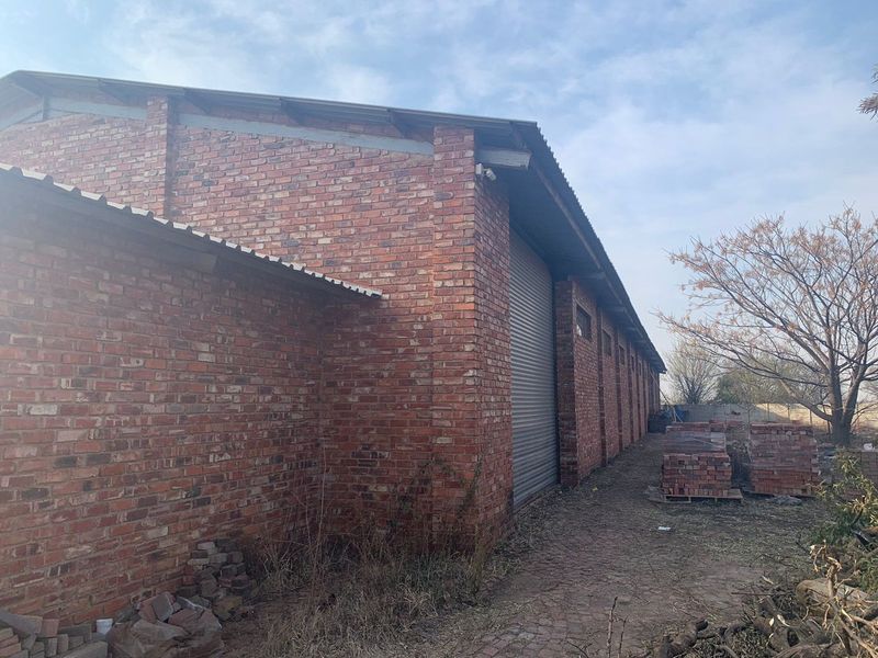 Exterior view of an industrial brick warehouse building featuring a metal roller shutter door and corrugated roofing.