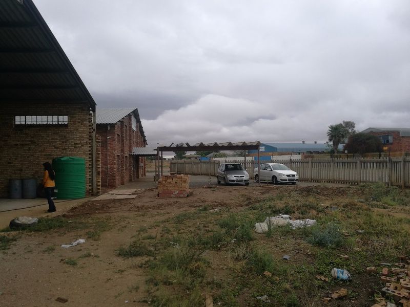 Industrial property exterior featuring a face brick warehouse building, corrugated roofing, a water storage tank, and an open yard area with a carport.