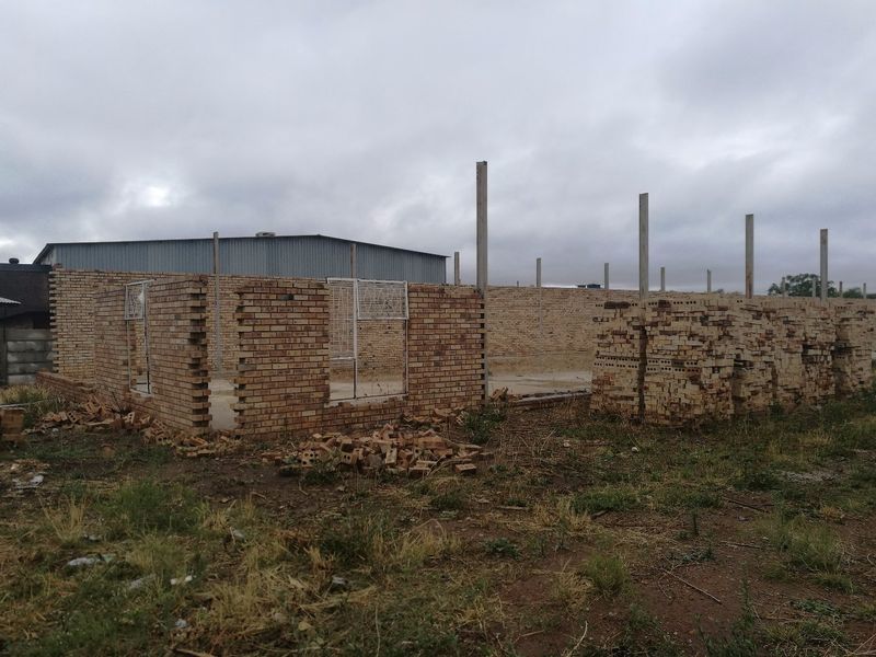 An industrial property under construction featuring exposed face brick walls, concrete columns, and a concrete slab foundation on a large plot.