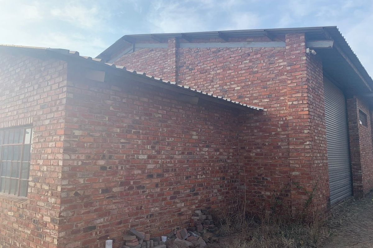 Exterior view of an industrial brick building featuring a corrugated metal roof and a secure roller shutter door.
