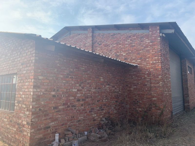 Exterior view of an industrial brick building featuring a corrugated metal roof and a secure roller shutter door.