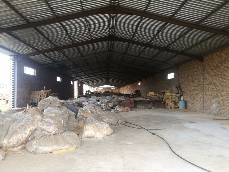Large industrial warehouse space featuring exposed brick walls, concrete flooring, and a high corrugated metal roof structure.