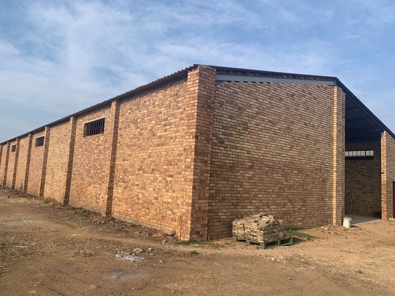 Exterior view of a large industrial warehouse building featuring face brick construction, corrugated metal roofing, and security-barred windows.