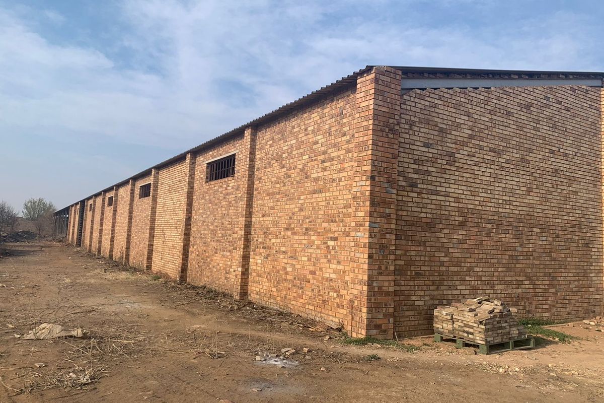 Exterior view of a large industrial warehouse building featuring face brick construction, corrugated metal roofing, and security-barred windows.