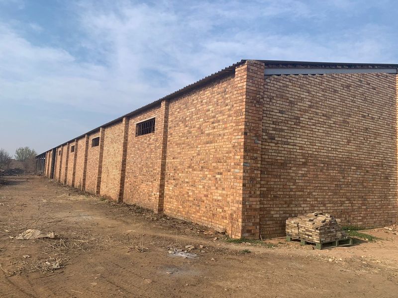 Exterior view of a large industrial warehouse building featuring face brick construction, corrugated metal roofing, and security-barred windows.