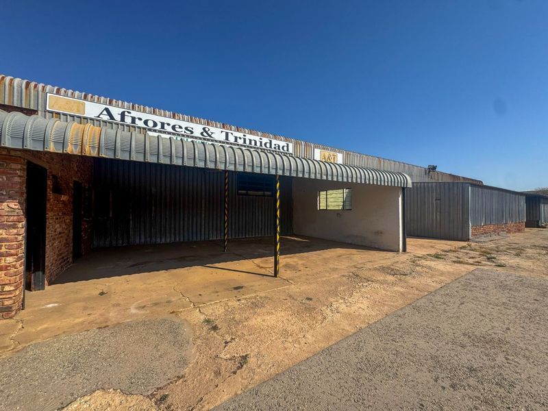 Industrial property exterior featuring corrugated metal roofing, brick masonry walls, and a concrete apron entrance area.