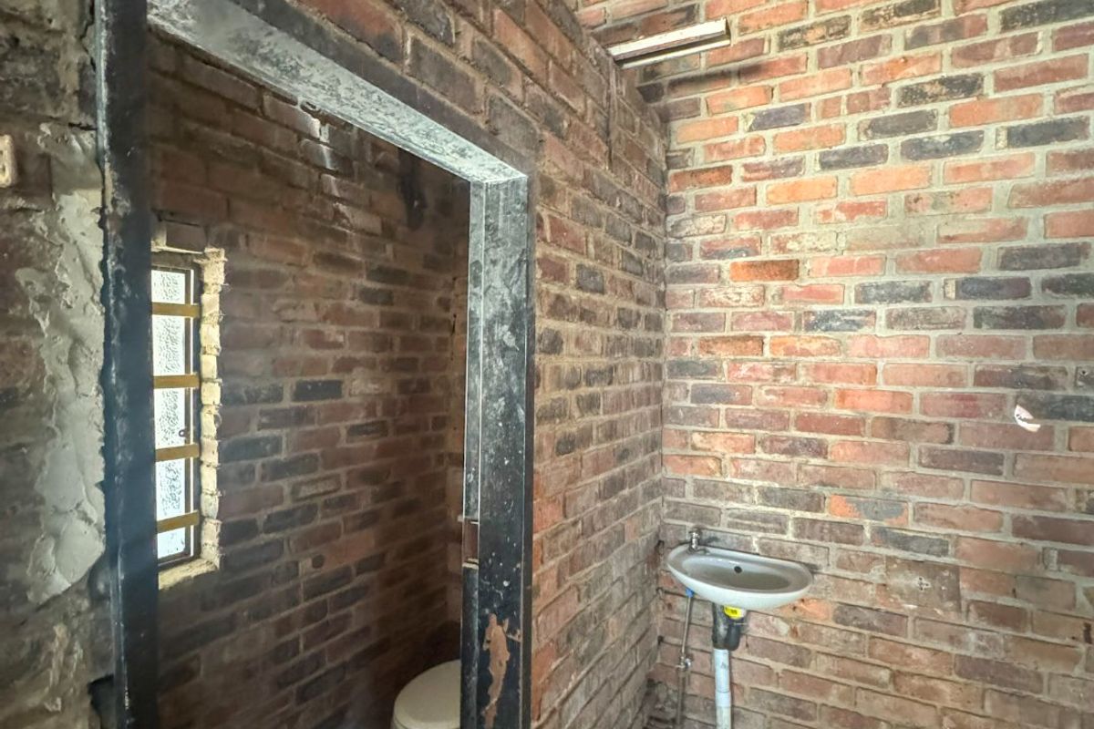An industrial-style bathroom space featuring exposed brick walls, a wall-mounted basin, and a toilet, currently in an unfinished shell condition.