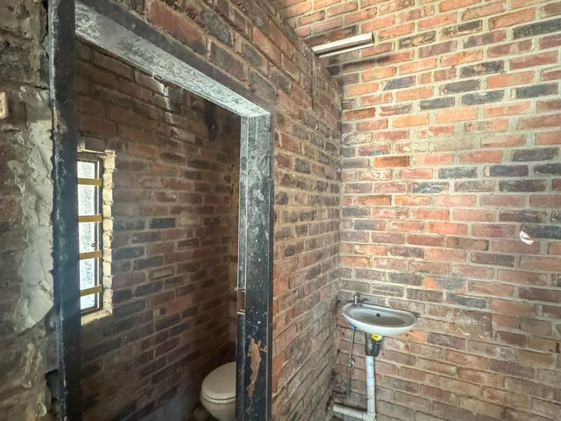 An industrial-style bathroom space featuring exposed brick walls, a wall-mounted basin, and a toilet, currently in an unfinished shell condition.