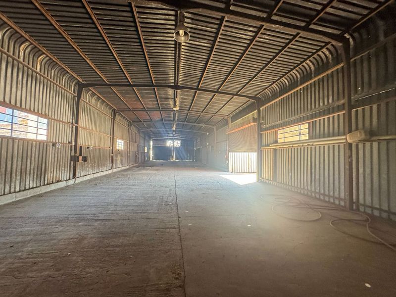 Spacious industrial utility area featuring corrugated metal walls, high ceilings, concrete flooring, and a large roller shutter door for easy access.