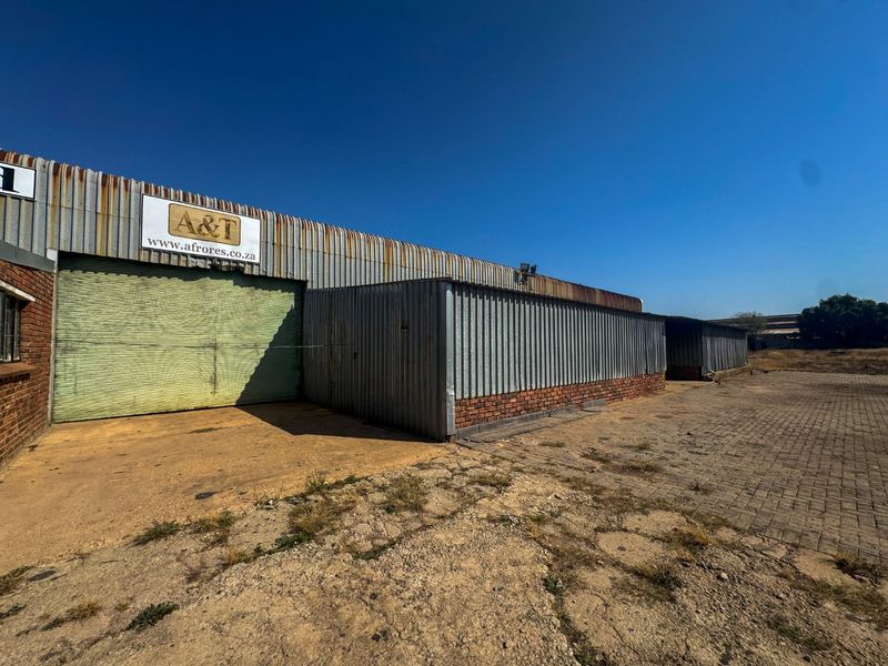 Industrial warehouse exterior featuring corrugated metal cladding, a large roller shutter door, and a paved yard area.