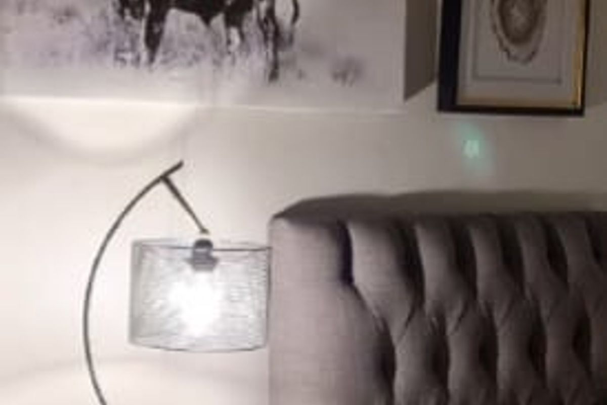 A close-up view of a bedroom corner featuring a tufted headboard and bedside lighting.