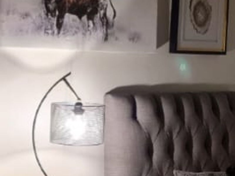 A close-up view of a bedroom corner featuring a tufted headboard and bedside lighting.