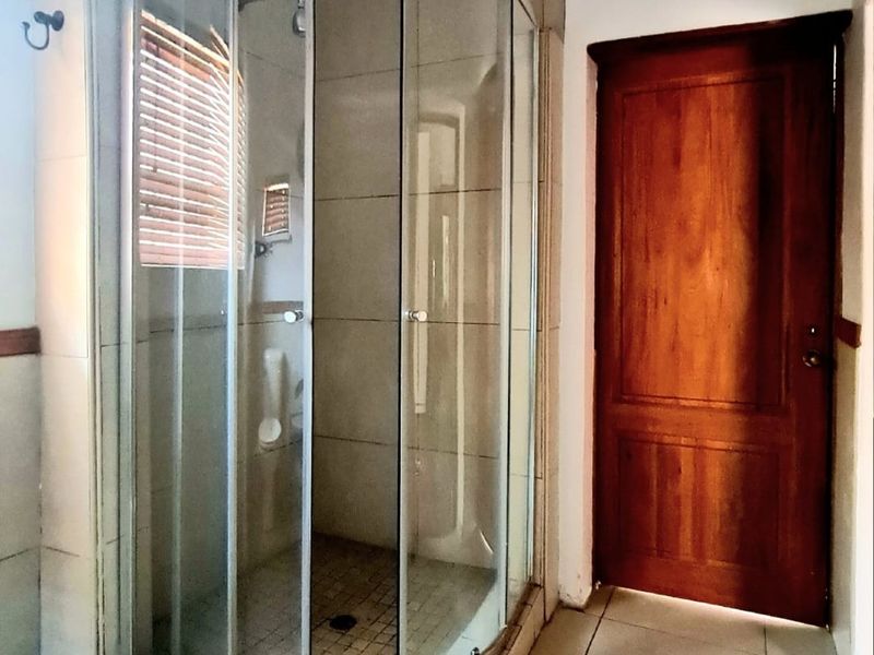 A functional bathroom featuring a curved glass shower enclosure with tiled finishes and a solid timber door.