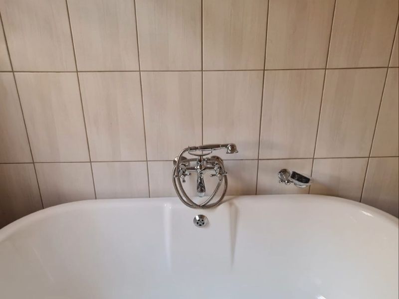 A clean bathroom featuring a modern white freestanding bathtub with a chrome telephone-style faucet and decorative mosaic tile border.