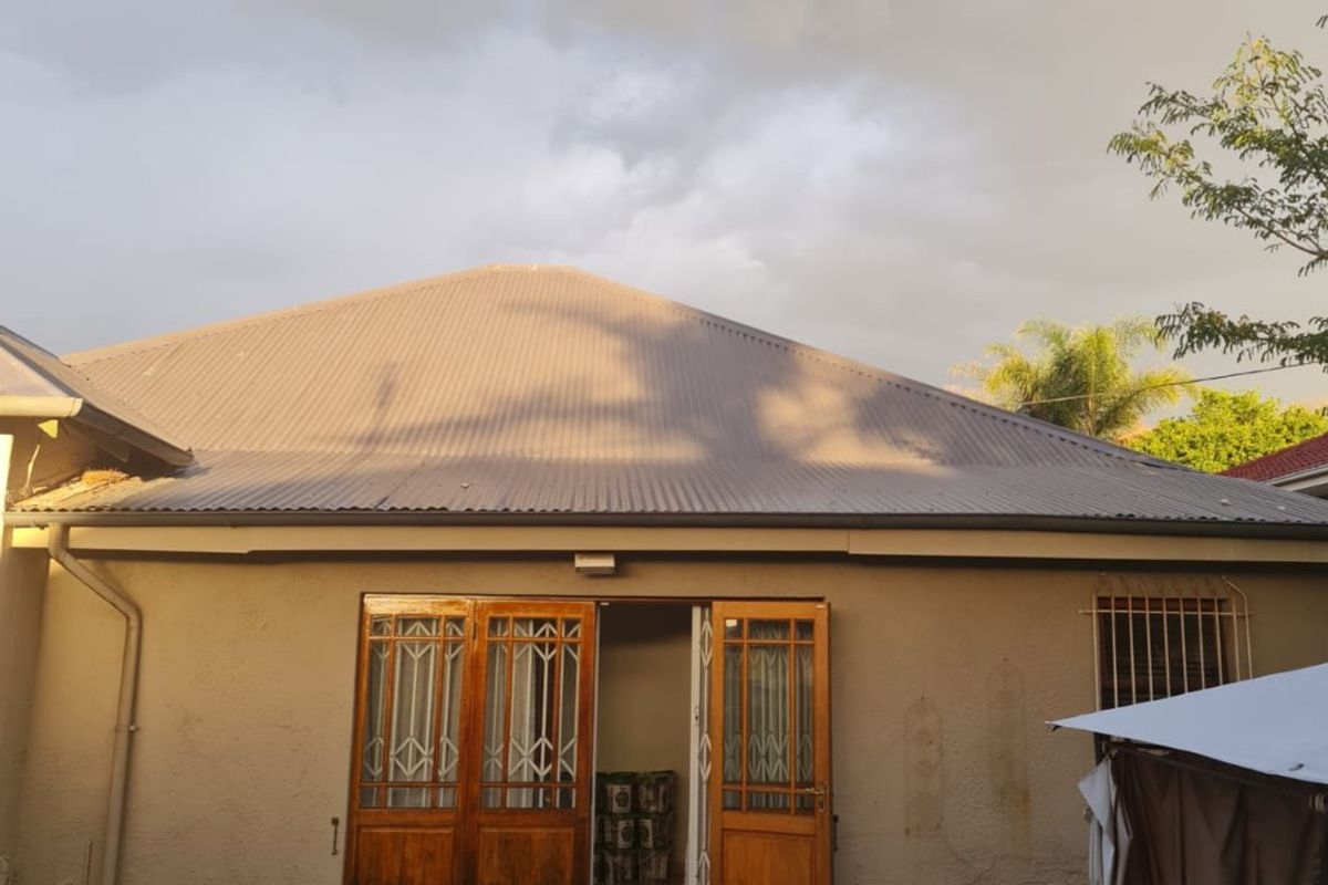 Rear view of the property featuring a corrugated metal roof, timber double doors with security gates, and tiled entrance steps leading to the garden.