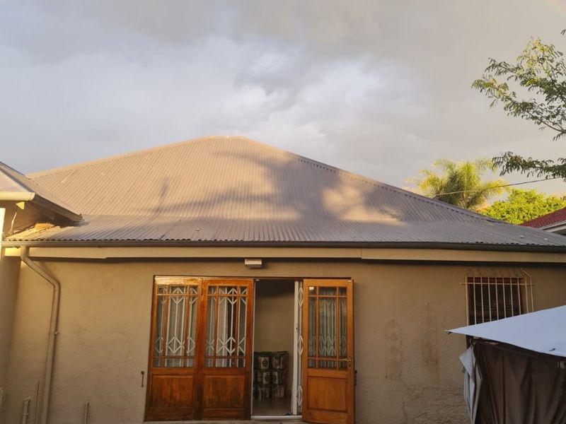Rear view of the property featuring a corrugated metal roof, timber double doors with security gates, and tiled entrance steps leading to the garden.