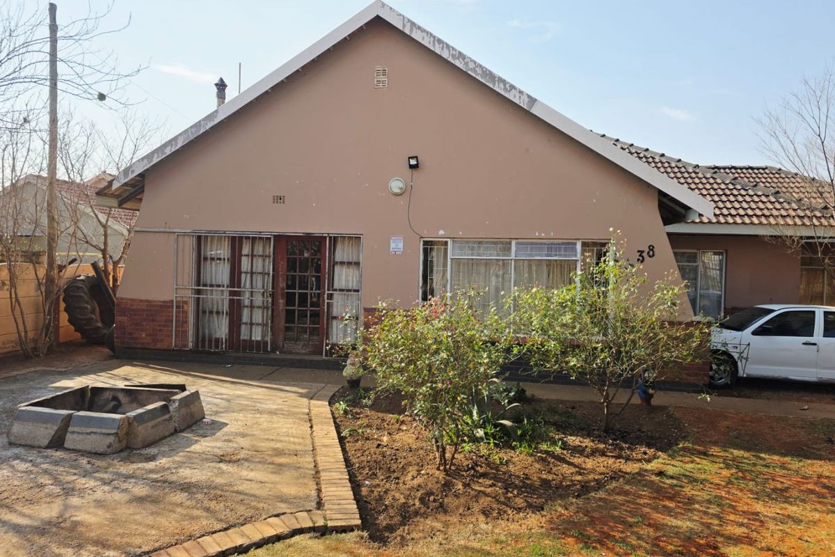 Rear exterior view of the house featuring a brick fire pit, security bars on windows, and a tiled roof structure.