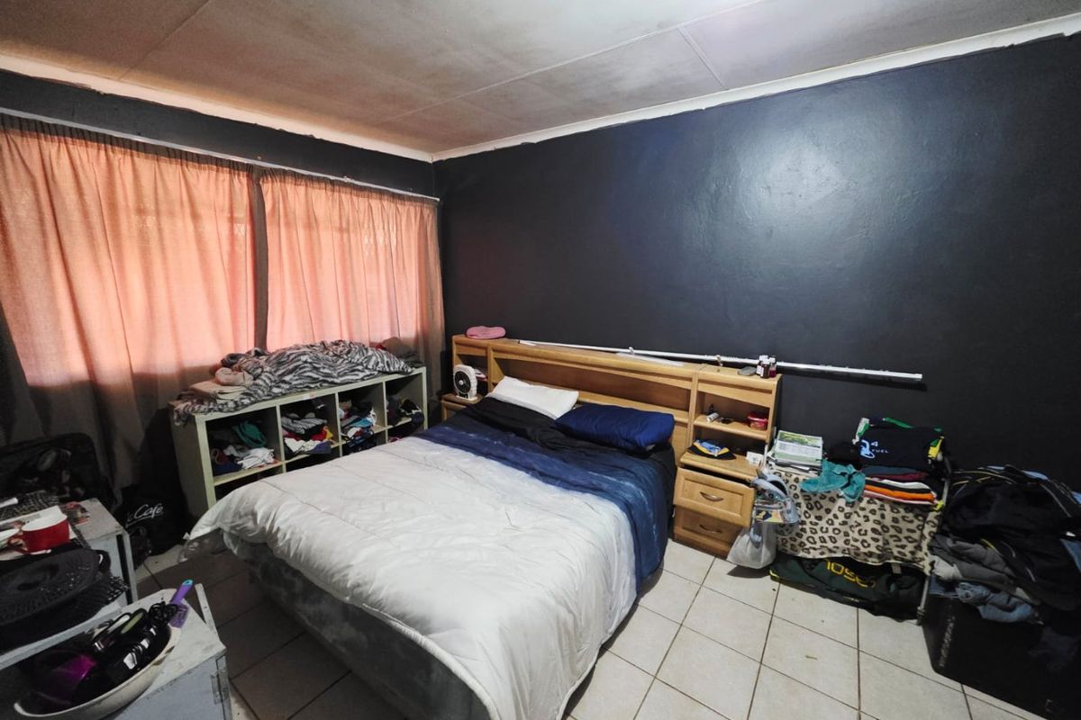 A bedroom featuring tiled flooring and a built-in headboard, currently requiring cosmetic updates to the ceiling and wall finishes.