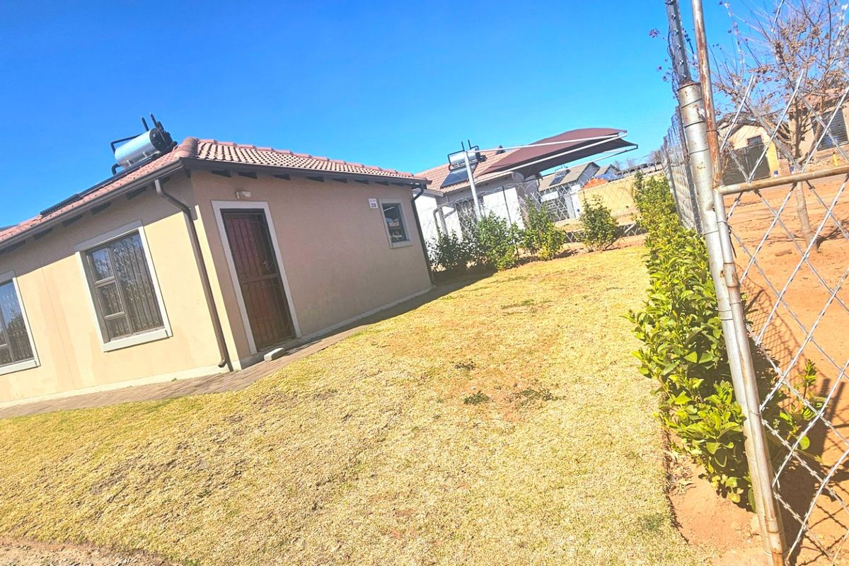 Rear view of a detached house featuring a tiled roof, solar geyser, and a fenced garden area.