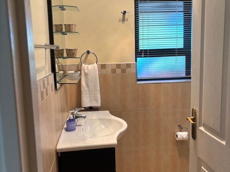 A functional bathroom featuring a vanity cabinet with a ceramic basin, tiled walls, and tiled flooring, complemented by a window with fitted blinds.