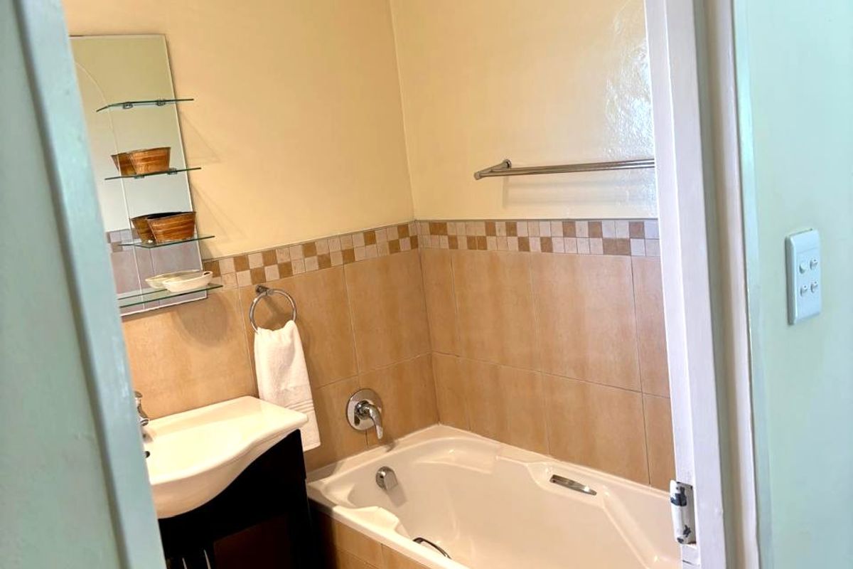 A functional bathroom featuring a built-in vanity, bathtub with tiled surround, and neutral wall tiling.