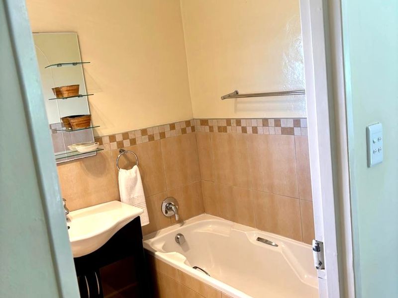 A functional bathroom featuring a built-in vanity, bathtub with tiled surround, and neutral wall tiling.