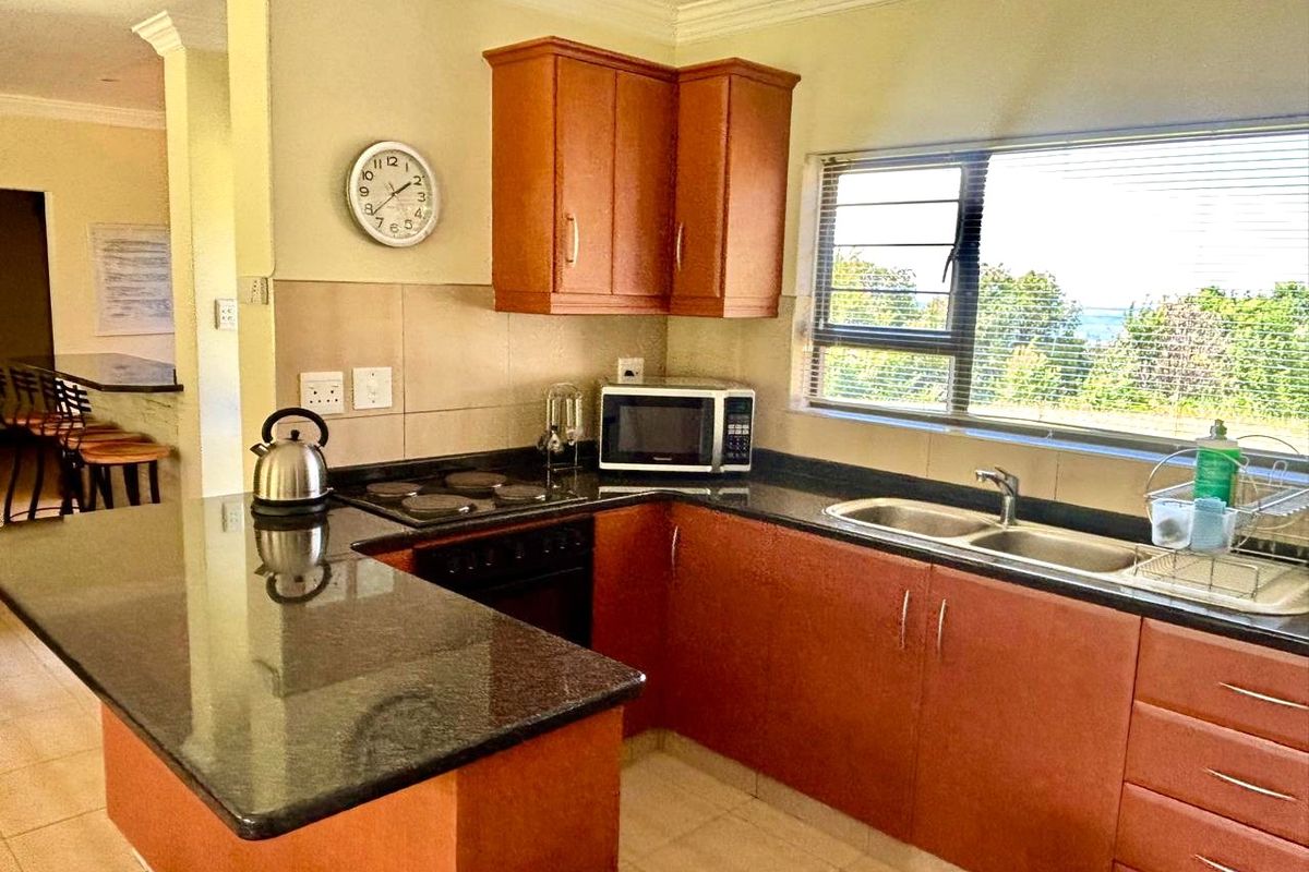 Functional kitchen featuring granite countertops, built-in cabinetry, electric hob, oven, and a double sink with a view through the window.
