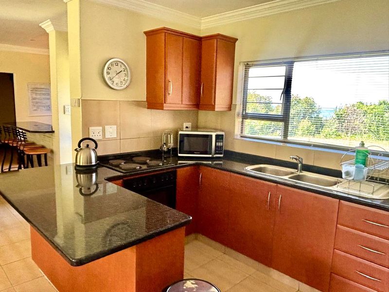 Functional kitchen featuring granite countertops, built-in cabinetry, electric hob, oven, and a double sink with a view through the window.