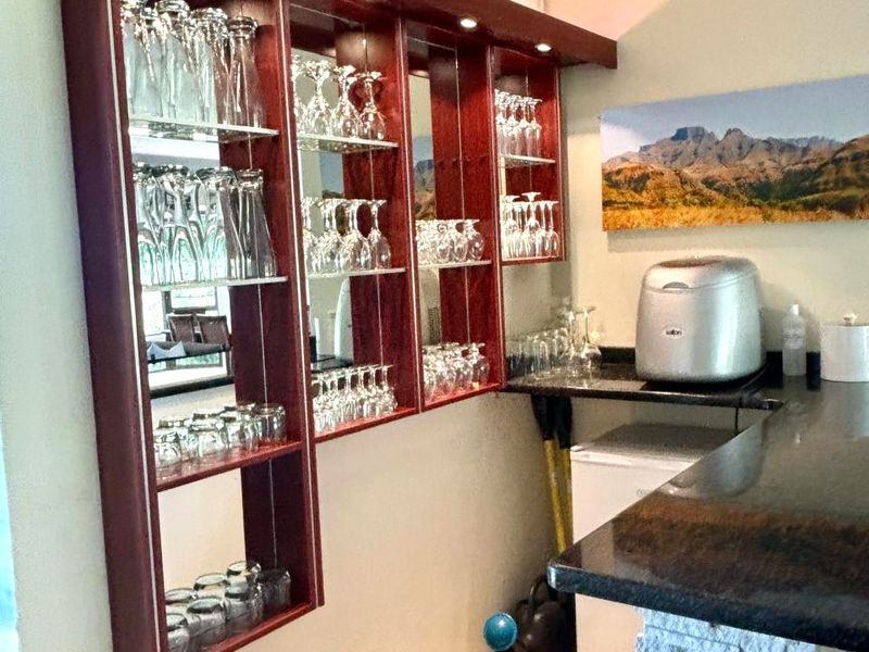 A dedicated home bar area featuring custom dark wood shelving with integrated lighting, mirrored backing, and a stone-clad counter with granite top.