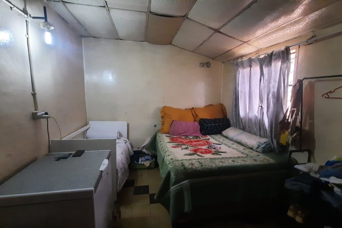 A bedroom featuring tiled flooring and a suspended ceiling with exposed electrical conduit, requiring cosmetic updates and repairs to finishes.