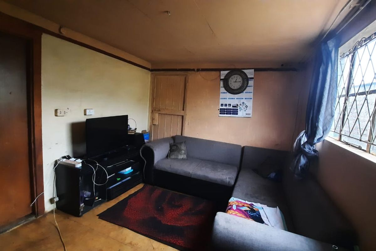 A living room area featuring security bars on the windows and a wooden door, requiring cosmetic updates to the walls and ceiling.