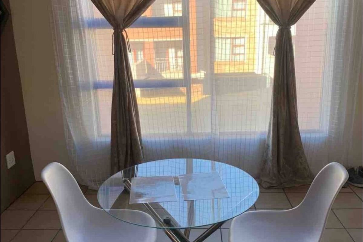 A bright living area featuring tiled flooring and a large window with natural light, suitable for a cozy dining or seating arrangement.
