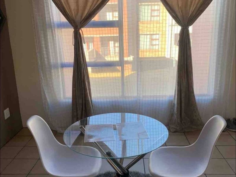A bright living area featuring tiled flooring and a large window with natural light, suitable for a cozy dining or seating arrangement.