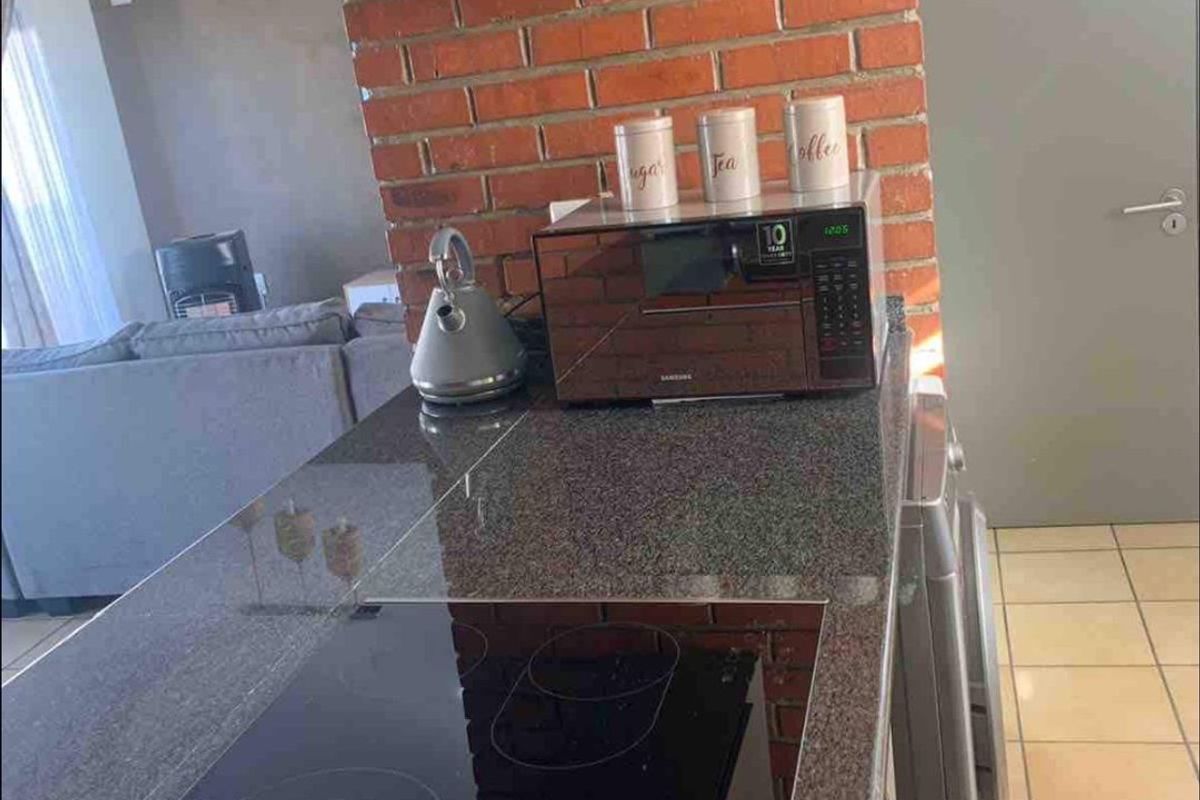 Compact kitchen area featuring granite countertops, an integrated electric hob, and a distinctive exposed brick pillar, seamlessly connecting to the living space.