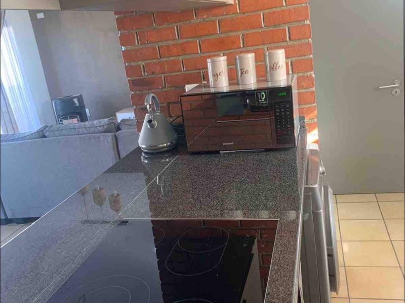 Compact kitchen area featuring granite countertops, an integrated electric hob, and a distinctive exposed brick pillar, seamlessly connecting to the living space.