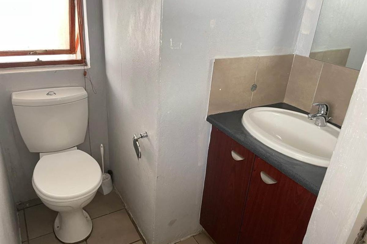 A compact bathroom featuring a standard toilet, vanity cabinet with basin, and tiled flooring, offering a functional space ready for cosmetic updates.