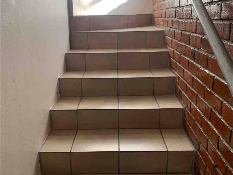 A staircase featuring tiled steps, an exposed brick feature wall, and a metal handrail leading to an upper level.