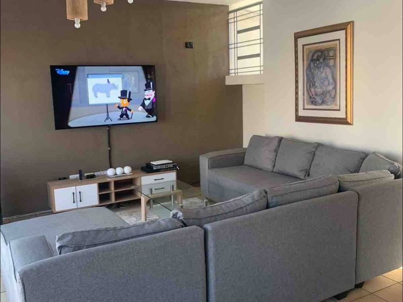 A comfortable living room featuring ceramic tile flooring, a neutral accent wall, and an open staircase leading to the upper level.