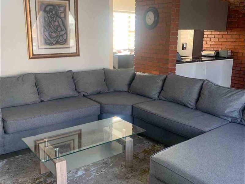 Open plan living area featuring tiled flooring and a distinctive exposed brick pillar separating the lounge from the kitchen space.