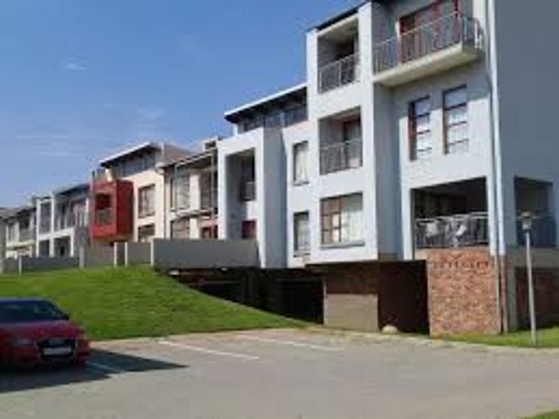 Exterior view of a modern apartment complex featuring multi-level balconies, brick detailing, and dedicated undercover parking spaces.