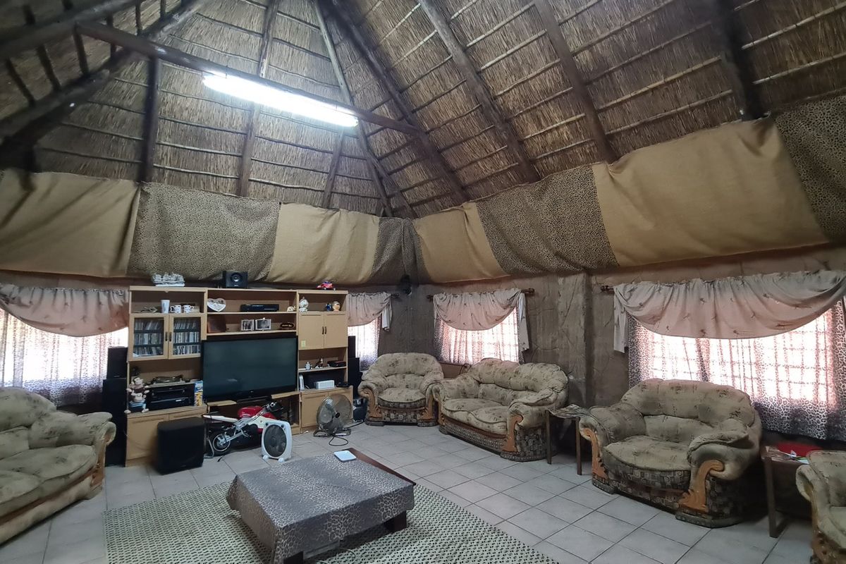 Spacious living area featuring a high vaulted thatch ceiling, tiled flooring, and large windows, offering a rustic and unique architectural aesthetic.
