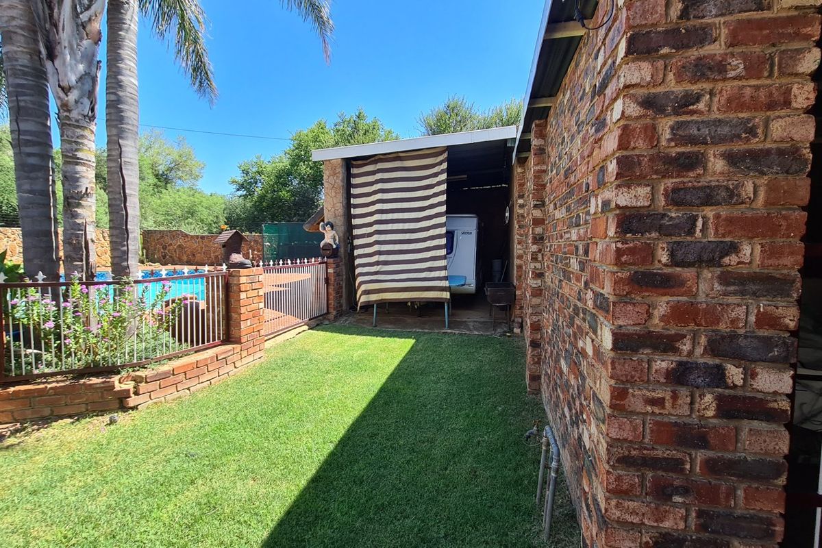 A side garden area featuring a brick exterior wall, a fenced swimming pool, and a covered storage space with a concrete floor.