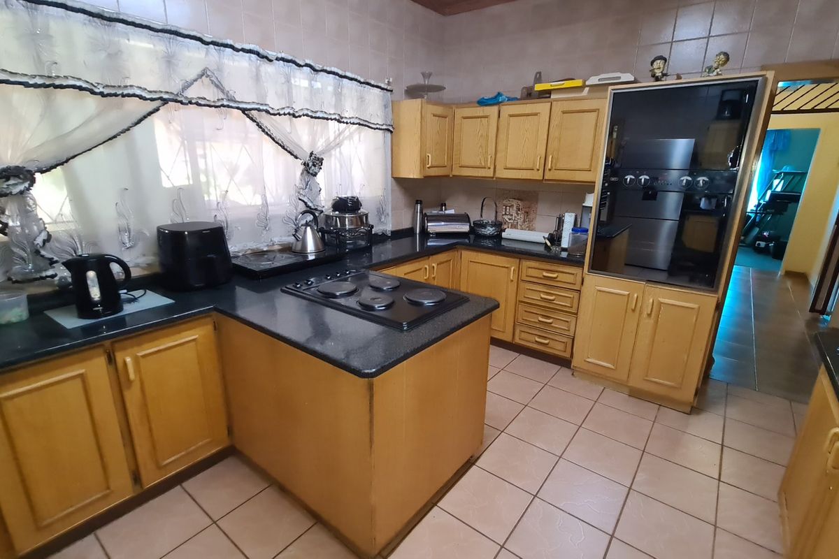 A functional kitchen featuring wooden cabinetry, dark countertops, a built-in oven, and a ceramic hob, finished with tiled flooring and wall surfaces.