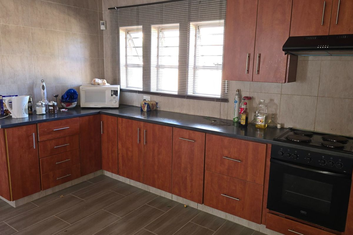 A functional kitchen featuring wood-look cabinetry, dark countertops, tiled walls, and a built-in oven with an extractor fan.