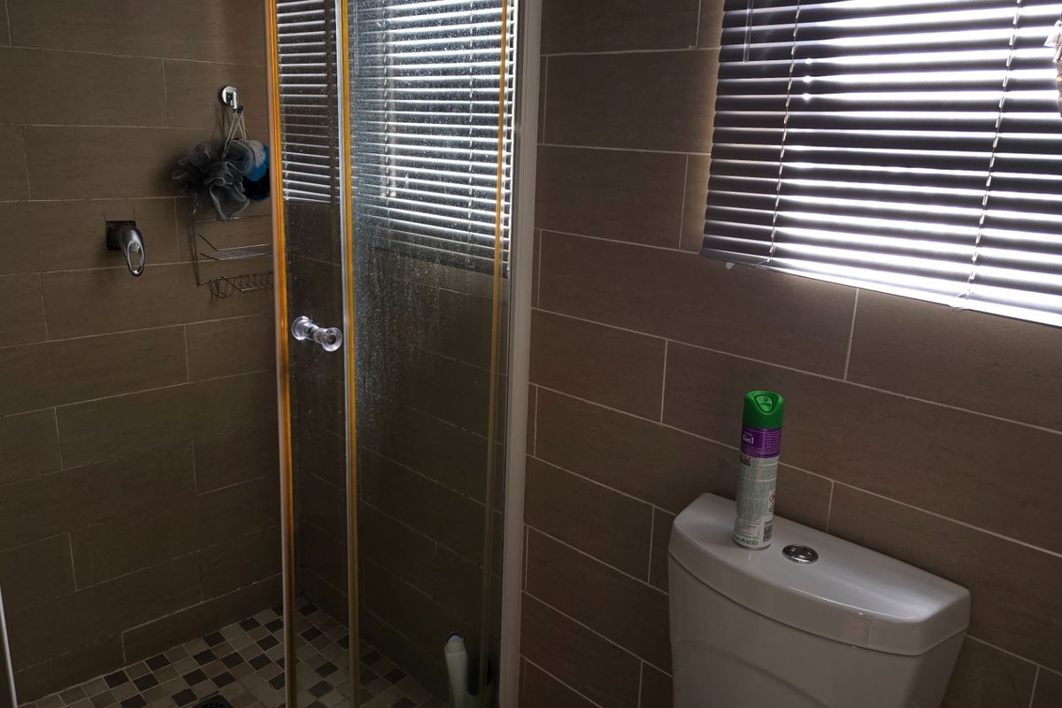 A compact bathroom featuring floor-to-ceiling tiled walls, a glass-enclosed shower, and a modern toilet with integrated window blinds.